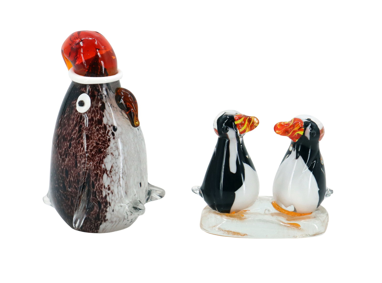 (2) Murano Style Art Glass Penguin Sculptures: (2) Murano Style Art Glass Penguin Sculptures. The larger whimsical one is shaped and colored like a baby Emperor penguin wearing a Santa Claus hat. The smaller one is formed like two squat penguins f