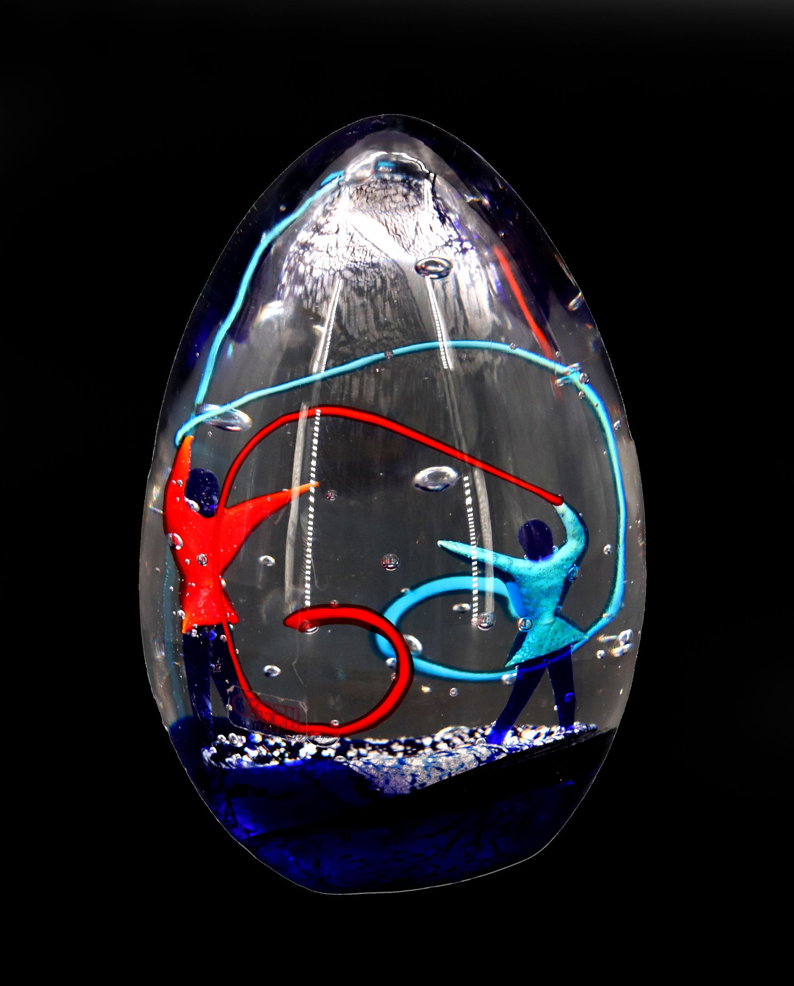 Roberto Camozzo (Born 1945) Italian, Ribbon Dancers Art Glass Egg Paperweight: Roberto Camozzo (Born 1945) Italian, Ribbon Dancers Art Glass Egg Paperweight. The egg form shows two figures, one blue, one red, dancing together with ribbons in a mostly clear space. Uncontrolled bu