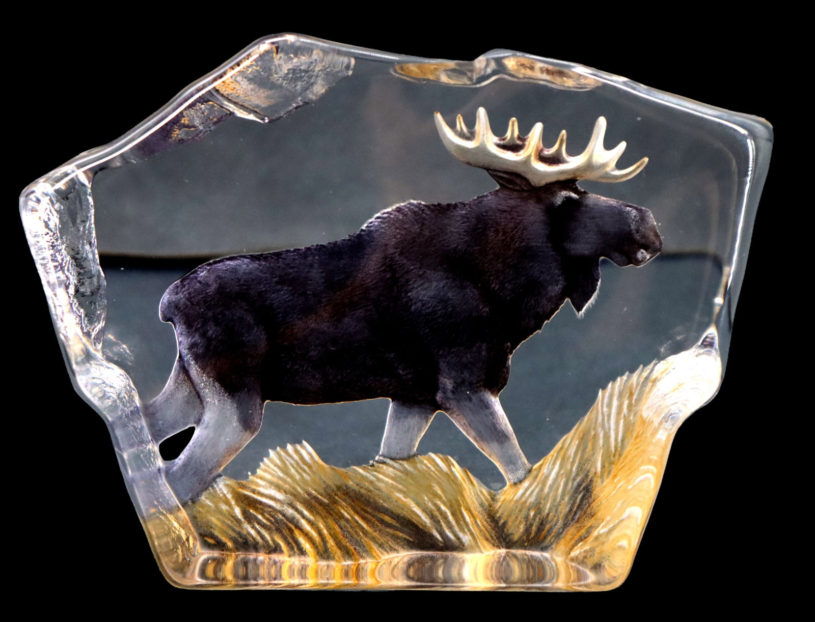 Mats Jonasson (Born 1945) Swedish, Maleras Painted Crystal Moose Paperweight: Mats Jonasson (Born 1945) Swedish, Maleras Painted Crystal Moose Paperweight. Signed on underside. Features a majestic bull moose traversing a golden patch of wild grass. The front of the sculpture is