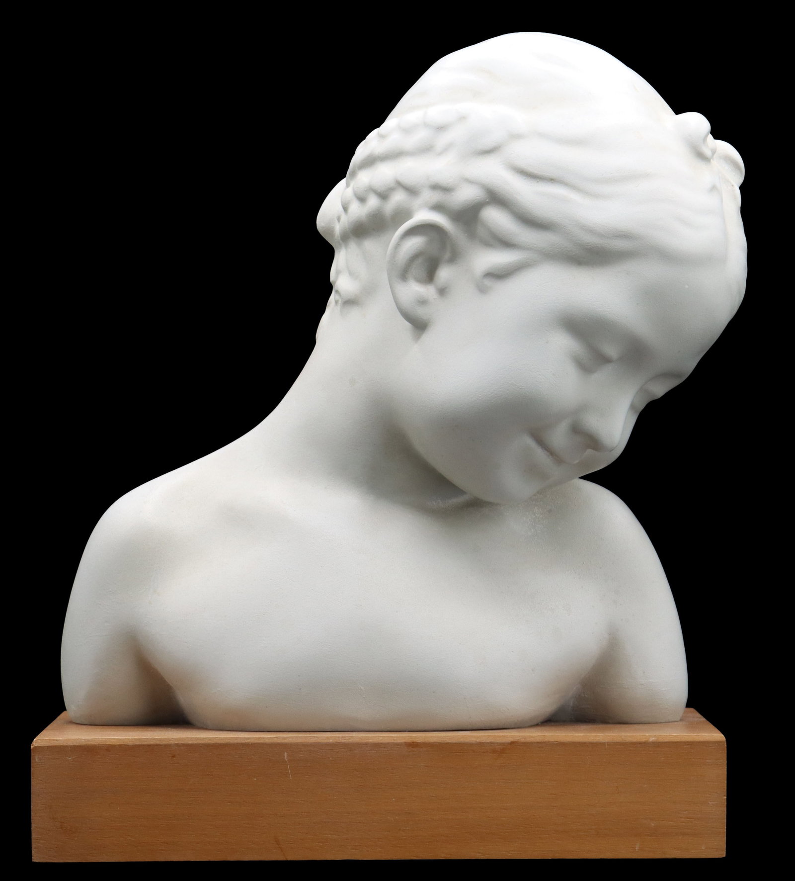Plaster Childs Bust on Wood Stand: Plaster Childs Bust on Wood Stand. The cast of the smiling young girl with her gaze turned down rests on a rectangular block of wood that has a small slightly descriptive label on the underside. 