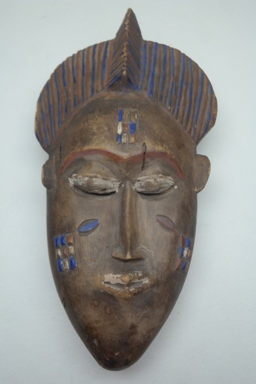 Antique Carved African Mask: Antique carved African mask in wood construction with slit eyes and diamond shaped mouth. Having painted accents in blue, brown and beige.