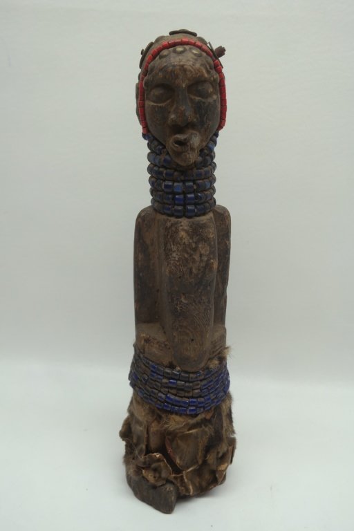 Antique Carved Figural Statue: Antique African carved figural statue in wood construction of female figure. Having red bead decoration to head and blue beaded decoration to neck and waist. Also with animal hide to bottom.