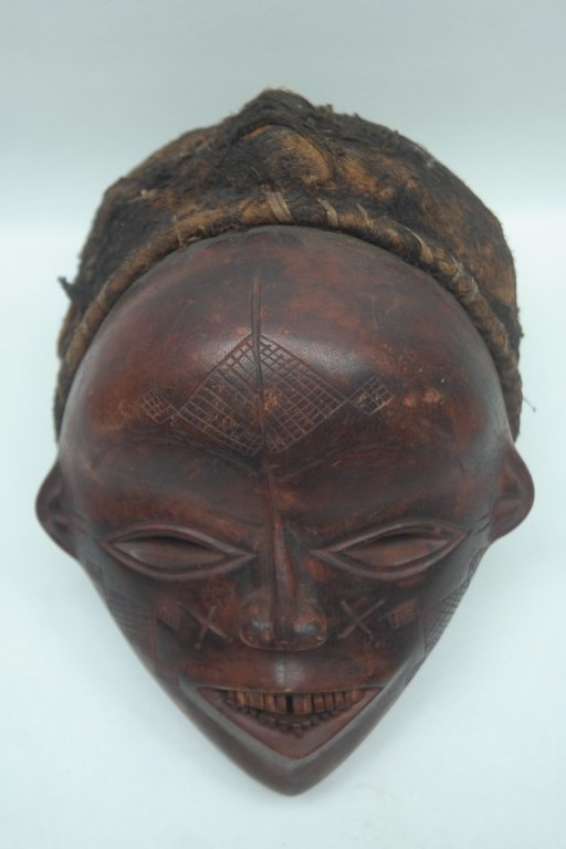 Antique Carved African Chokwe Mask: Antique carved African Chowke mask in wood construction having almond shaped eyes and diamond shaped mouth with stylized teeth. Face is decorated with carvings. Also with hide head covering.