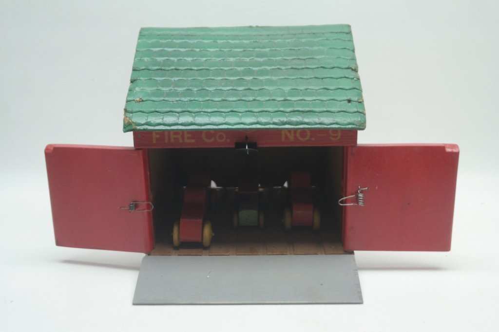 20th C. Wooden Fire Station: Circa 1930s wooden fire station, with cars and bell. Cars can be shot out through fire station doors, by lever system. With two fire trucks, has room for third car. Fire station has been reconstructed