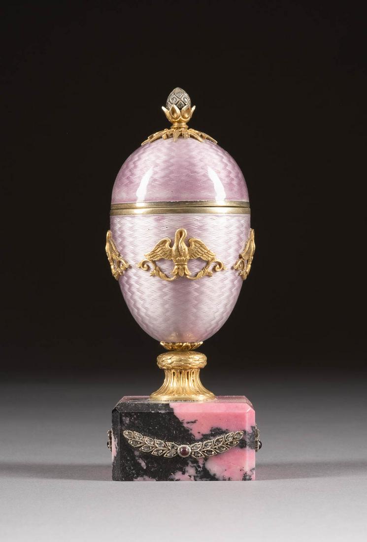 A SILVER-GILT AND CHAMPLEVÉ ENAMEL EGG-SHAPED BOX WITH: A SILVER-GILT AND CHAMPLEVÉ ENAMEL EGG-SHAPED BOX WITH CASE 2nd half 20th century On a rhodonite base. Bearing spurious Russian hallmarks. Enamel chipped. 11.7 cm high. GUILLOCHÉ-EMAIL-DOSE IM ETUI