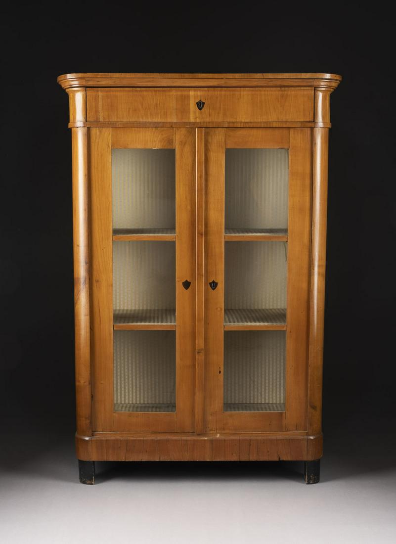 BIEDERMEIER-VITRINENSCHRANK: BIEDERMEIER-VITRINENSCHRANK Deutsch, um 1820/ 1830 Kirsche, furniert, teils ebonisiert. H. 152,5 cm, B. 104 cm, T. 50 cm. Hochrechteckiger, zweitueriger Korpus mit dreiseitiger Verglasung und abgerund
