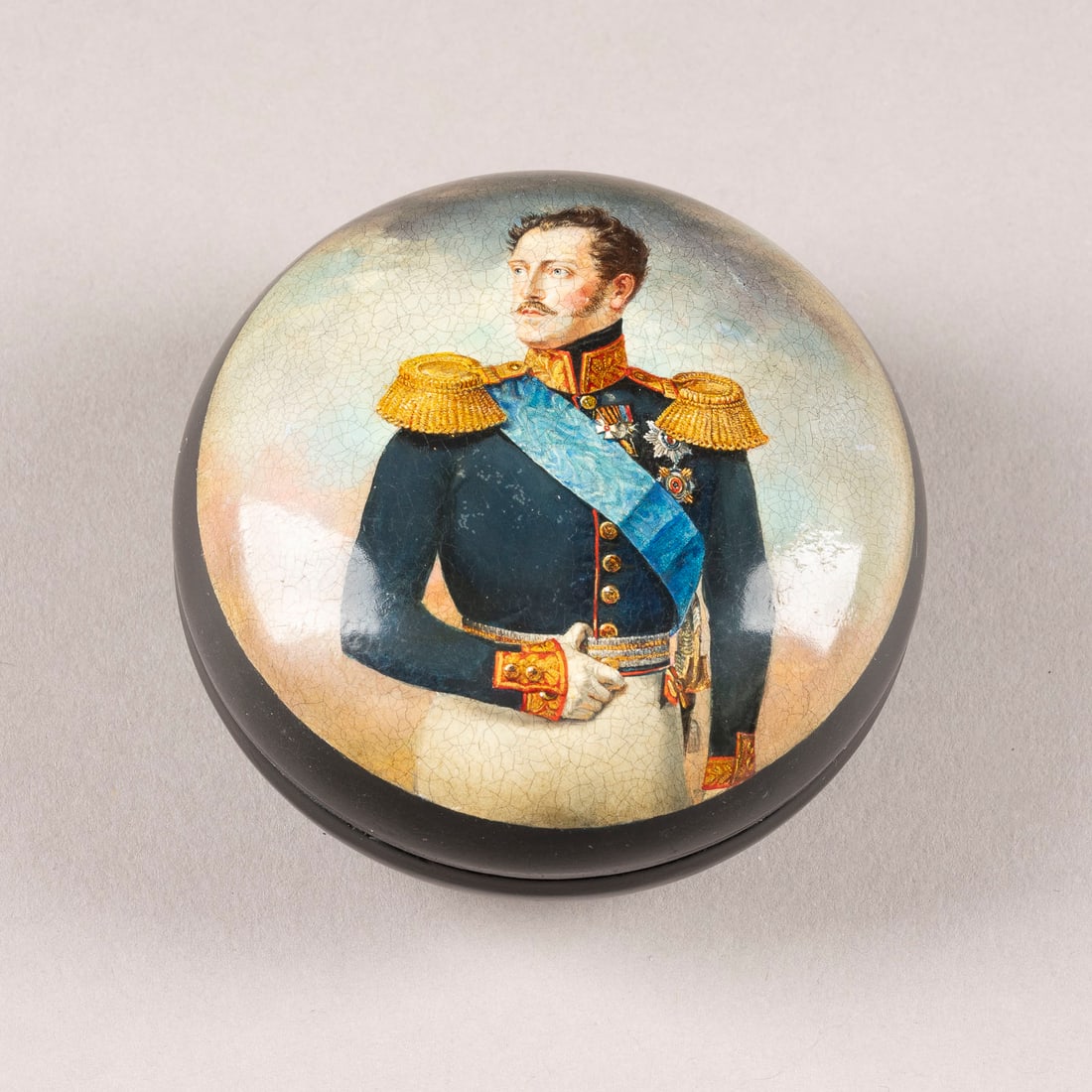 A PAPIER-MACHE AND LACQUER BOX WITH A PORTRAIT OF EMPEROR NICHOLAS I AFTER FRANZ KRUEGER: A PAPIER-MACHE AND LACQUER BOX WITH A PORTRAIT OF EMPEROR NICHOLAS I AFTER FRANZ KRUEGER Russian, Ostashkovo, Vishnyakov Factory, 1882-1888 Of circular form. The red lacquered interior signed with fir