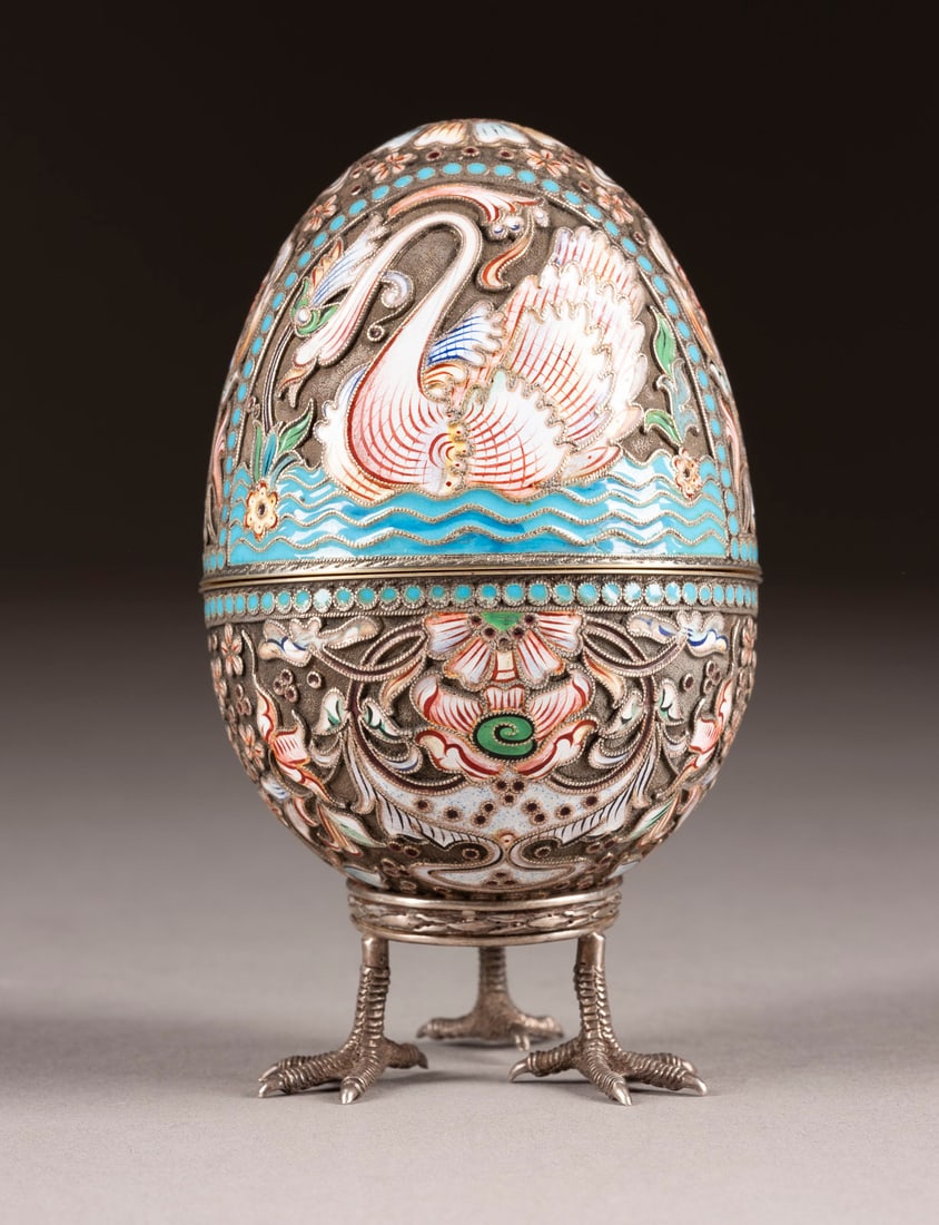 A SILVER AND CLOISONNE ENAMEL EGG ON STAND: A SILVER AND CLOISONNE ENAMEL EGG ON STAND 2nd half 20th century Ovoid, in two halves, enamelled with bands of stylized foliage and flowers and geometric motifs, within pale blue pellet borders. Beari