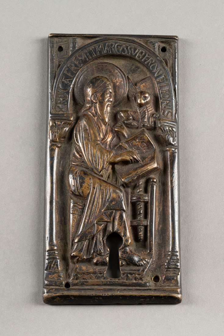 DEUTSCHER BILDPLASTIKER HEILIGER MARKUS AM SCHREIBPULT: GERMAN SCULPTOR Romanesque style SAINT MARKUS AT WRITING DESK Bronze, dark patinated, with key-shaped opening. H. 13, w. 6,5, d. 1 cm, weight ca. 204g. Verso Luchtenberg collection inventory number 'B