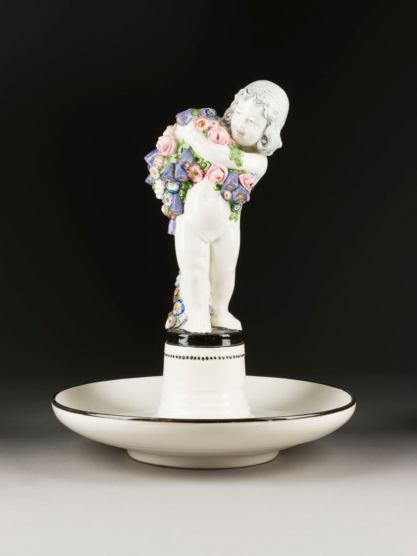 CARL KLIMT GROSSER TAFELAUFSATZ MIT PUTTO: CARL KLIMT 1876 Teplitz - 1945 Zinnwald GROSSER TAFELAUFSATZ MIT PUTTO Oesterreich, Ausfuehrung wohl Bernhard Bloch, Eichwald, Boehmen, um 1910 Keramik, heller Scherben, glasiert, polychrom bemalt. H.