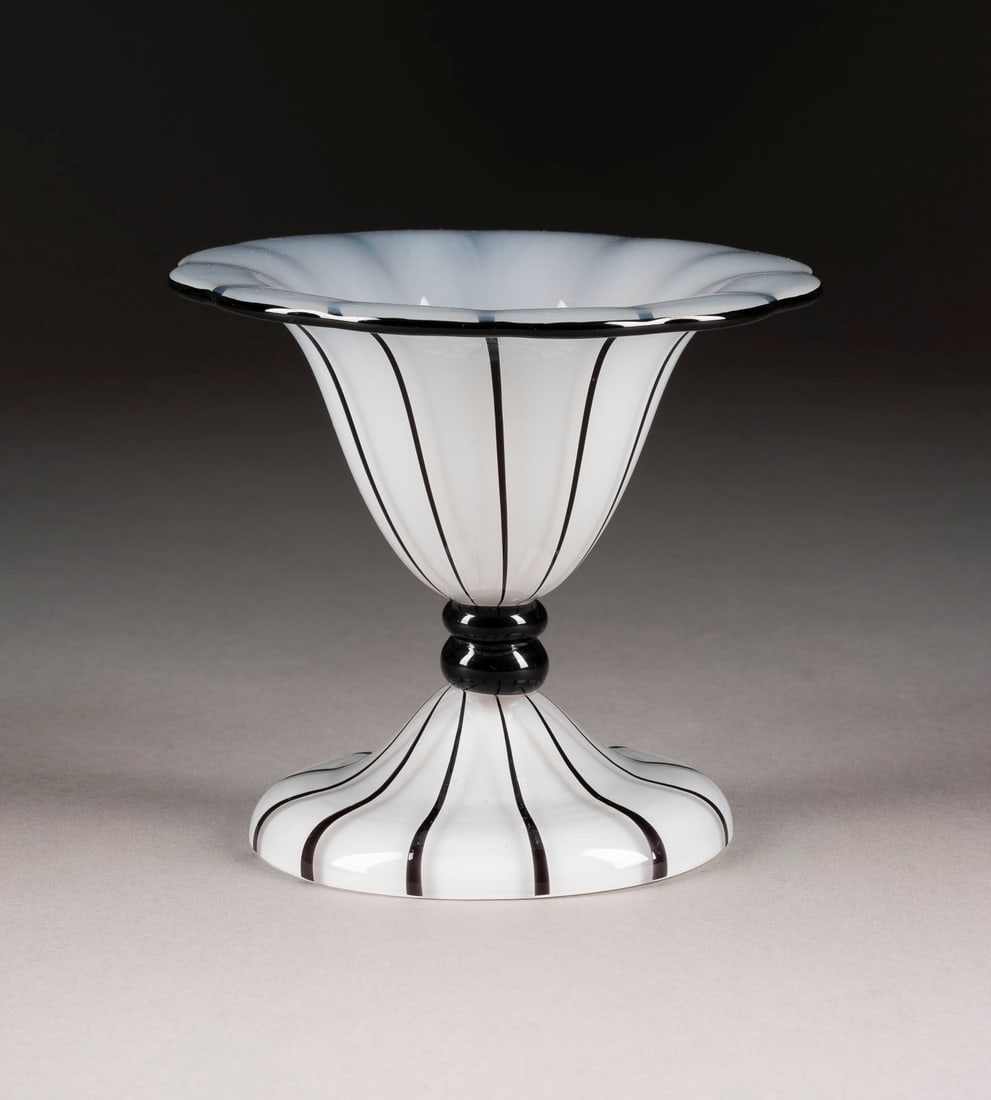 KLEINE FUSSSCHALE: KLEINE FUSSSCHALE Boehmen, Klostermuehle, Loetz Witwe, Michael Powolny (Entwurf), um 1914 Opalweisses Ueberfangglas, vertikaler Streifendekor aus schwarzen Fadenauflagen. H. 11,7 cm, D. 13,5 cm. Ausfu