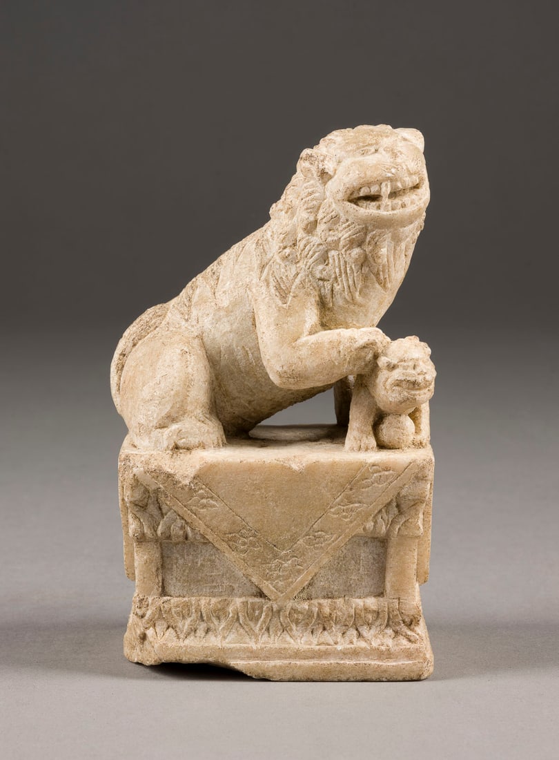 EINE GESCHNITZTE FIGUR EINES BUDDHISTISCHEN LÖWEN AUS STEIN: A STONE CARVED FIGURE OF BUDDHIST LION China Stone. H. 13.5 cm. With traces of use and age, partially damaged and chipped.EINE GESCHNITZTE FIGUR EINES BUDDHISTISCHEN LÖWEN AUS STEIN China Stein. H. 1