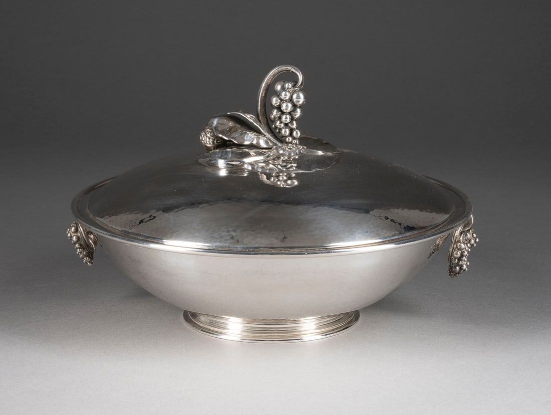| ART-DÉCO GEMÜSETERRINE MIT TRAUBEN VON GEORG JENSEN: ART-DÉCO GEMÜSETERRINE MIT TRAUBEN VON GEORG JENSEN Dänemark, Georg Jensen, 1981, (Entwurf um 1925) 925er Silber. H. 16 cm, D. 24 cm, Gew. 1490 g. Punziert mit Herstellermarke, Feingehaltsangabe '9