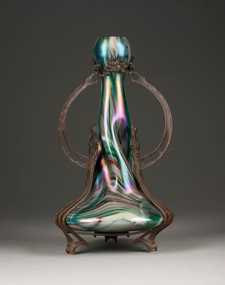 | JUGENDSTIL-VASE MIT METALLMONTIERUNG: JUGENDSTIL-VASE MIT METALLMONTIERUNG Wohl Tschechische Republik, um 1900 Farbloses Glas, violetter, blauer, grüner und weißer gekämmter Dekor, irisierend, Metallmontierung. H. 34,5 cm. Innenkante