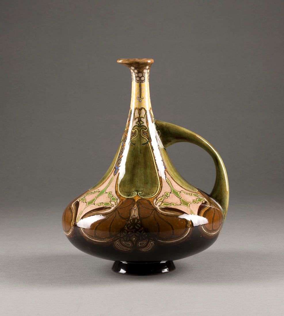 | JUGENDSTIL-HENKELKANNE MIT BLUMENMALEREI: JUGENDSTIL-HENKELKANNE MIT BLUMENMALEREI Niederlanden, Den Haag, Rozenburg, um 1900 Keramik, heller Scherben, farbig bemalt. H. 28,5 cm. Im Boden Pinselmarke (undeutlich), '... M.A?' (eingeritzt