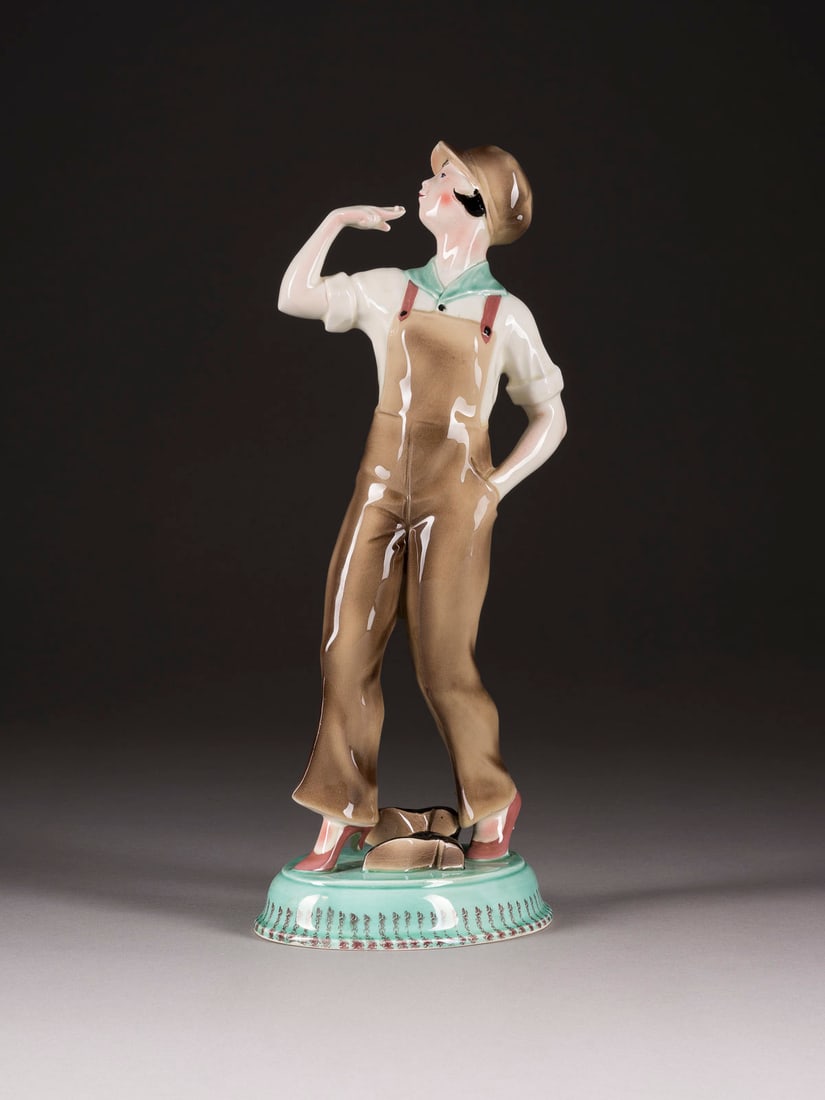 | ART-DECO-FIGUR 'FRAU IN LATZHOSEN': ART-DECO-FIGUR 'FRAU IN LATZHOSEN' Um 1930 Keramik, heller Scherben, polychrom gefasst. H. 38 cm. Eingepresst 'M'. Zigarette besch., Schirm am Rand min. best.ART-DECO-FIGUR 'FRAU IN LATZHOSEN'