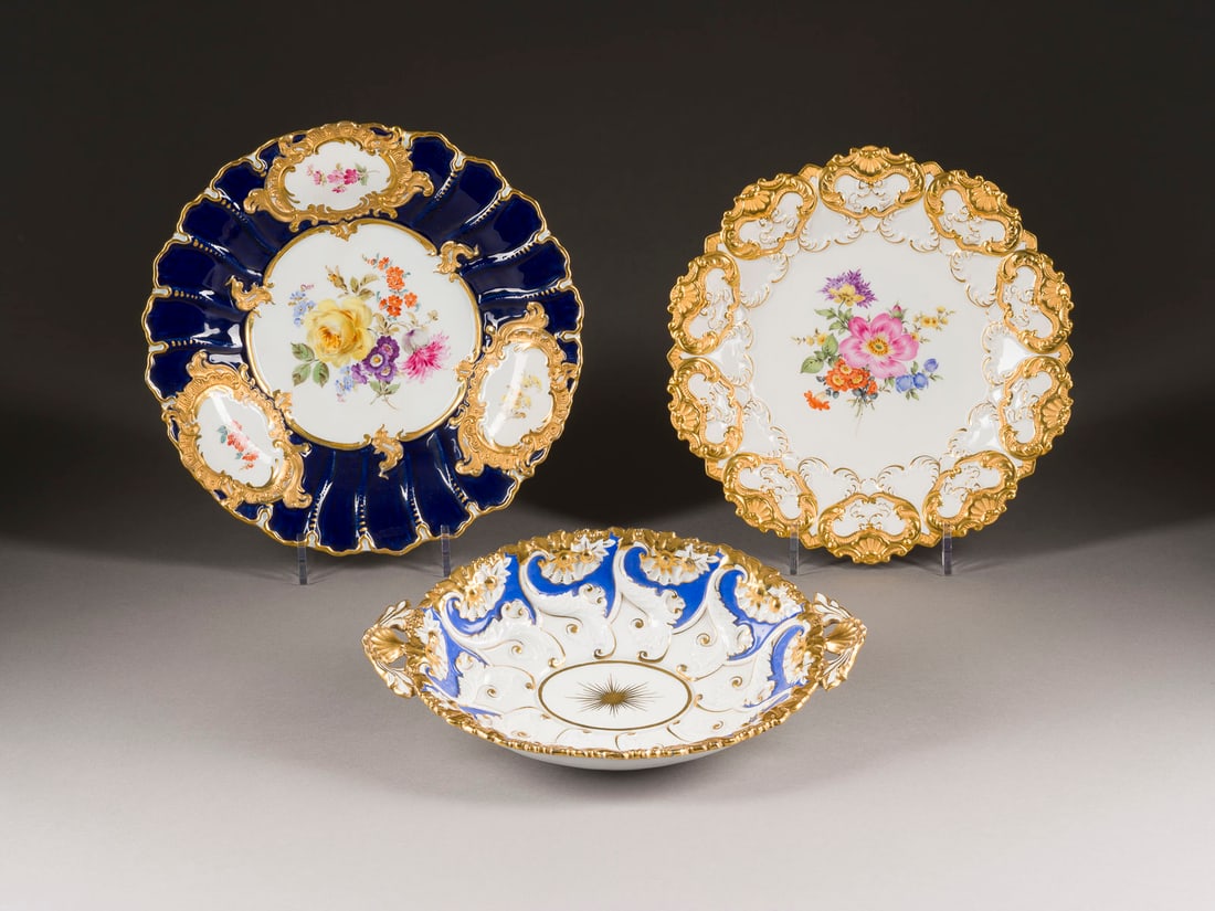 | ZWEI PRUNKTELLER UND EINE PRUNKSCHALE: ZWEI PRUNKTELLER UND EINE PRUNKSCHALE Deutsch, Meissen, 20. Jh. Porzellan, teilw. polychrome Malerei, teilw. kobaltblauer Fond, glänzende und matte Goldstaffage. L. 30,5 cm, D. 27,5-29,5 cm. Untergla