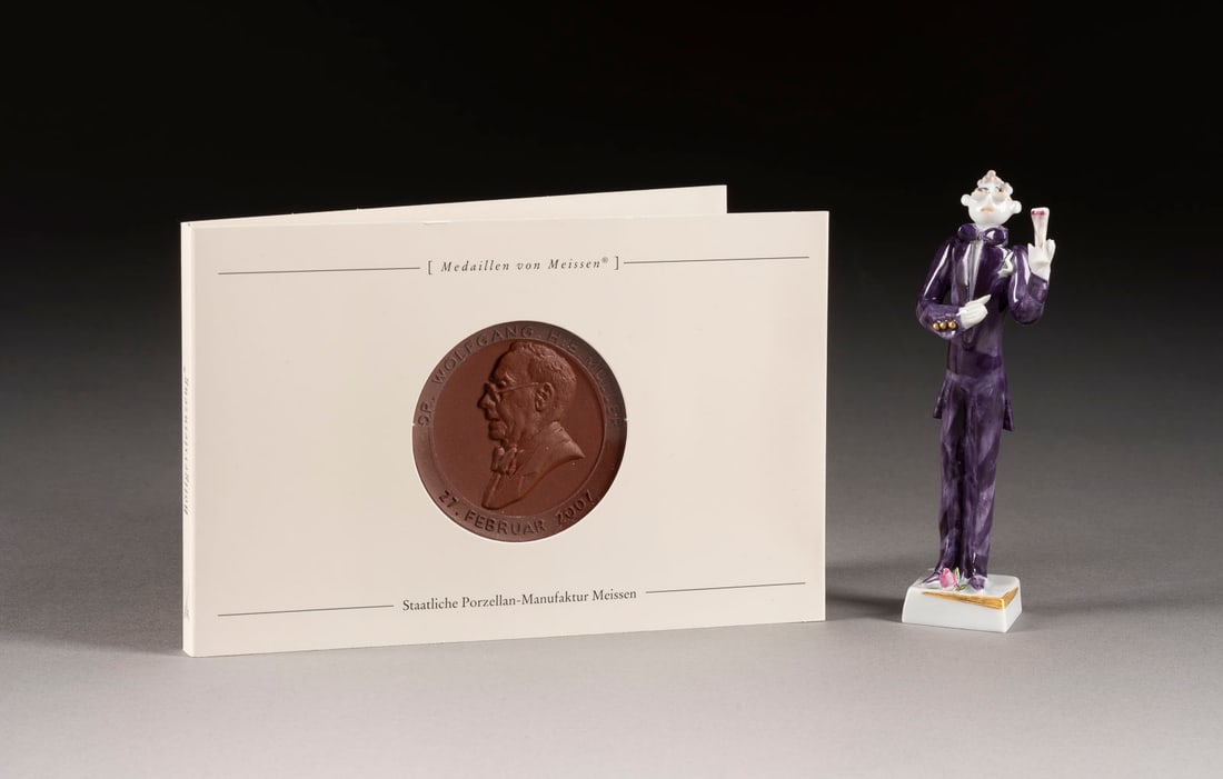 | MINIATURFIGUR UND GEDENKMEDAILLE 'DR. MÜLLER': MINIATURFIGUR UND GEDENKMEDAILLE 'DR. MÜLLER' Deutsch, Meissen, 2007 Böttgersteinzeug, Porzellan, polychrome Malerei, dezente Goldstaffage. H. 10,5 cm, D. 5 cm. Unterglasurblaue und reliefierte