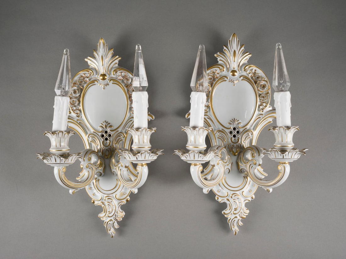 | PAAR WANDLEUCHTER IM BAROCKSTIL: PAAR WANDLEUCHTER IM BAROCKSTIL Deutsch, Dresden, Sandizell Porzellan, 20. Jh. Weißporzellan, Goldstaffage, elektrifiziert (Funktion nicht geprüft). H. 41,5 cm. Auf Ruckseite D unter Krone 'Reine