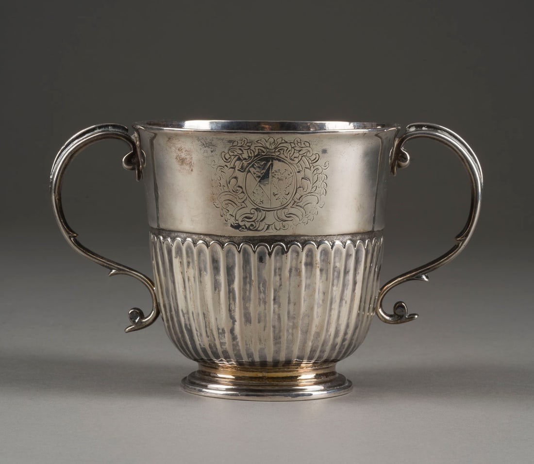 | QUEEN ANNE-BECHER MIT ZWEI HENKELN: QUEEN ANNE-BECHER MIT ZWEI HENKELN England, London, John Fawdery, 1703 Sterlingsilber, part. vergoldet. H. 10,4 cm, 300 g. Punziert mit Garantiemarke, Feingehaltsangabe, Meistermarke 'FA' sowie