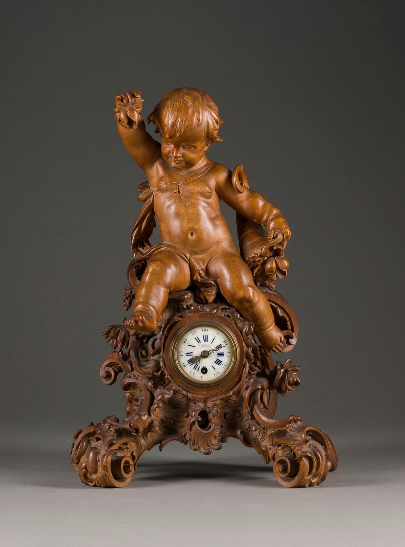 | TISCHUHR MIT PUTTO: TISCHUHR MIT PUTTO Deutsch, F. Schlesicky, Frankfurt, um 1860 Holz, geschnitzt, Metall, Email. 39 x 27 x 15 cm. Auf dem Zifferblatt bez. 'F. Schlesicky Frankfurt'; auf dem Werk bez. 'F. Schlesicky