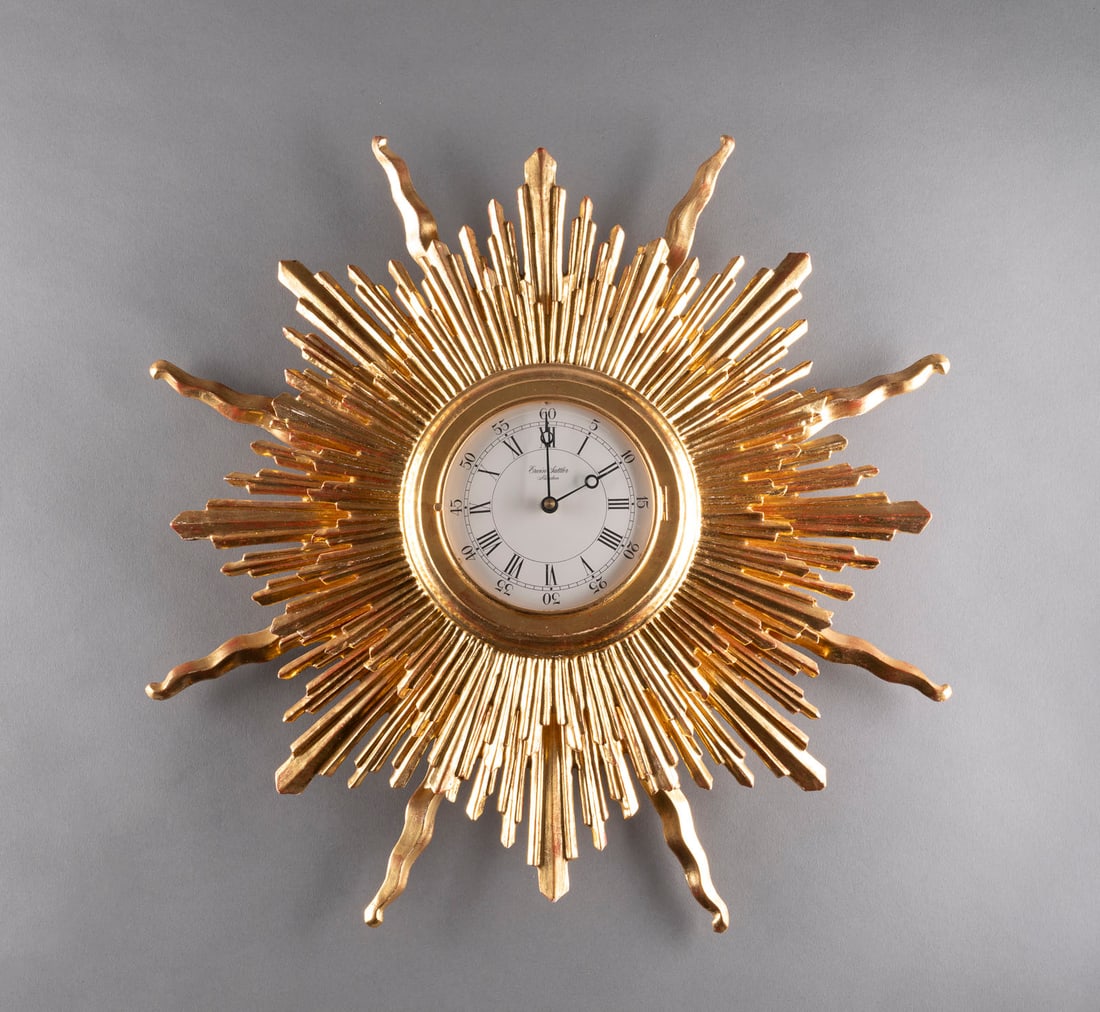 | ERWIN SATTLER WANDUHR 'SONNE': ERWIN SATTLER WANDUHR 'SONNE' Deutsch, München, Erwin Sattler, 20. Jh. Holz, vergoldet, Glas, Stahl, Kunststoff. H. ca. 10 cm, D. ca. 52 cm. Auf dem Zifferblatt bez. 'Erwin Sattler München'. Hinter