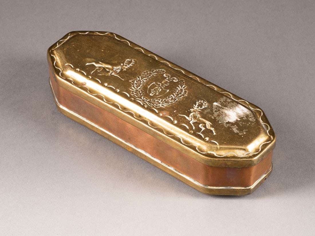 | ISERLOHNER TABAKSDOSE: ISERLOHNER TABAKSDOSE Deutsch, 2. Hälfte 18. Jh. Messing, Kupfer. 14,5 x 5,5 x 3,5 cm. Längsrechteckige Form mit abgeschrägten Kanten und scharniertem Messingdeckel sowie Messingboden. Deckel mit