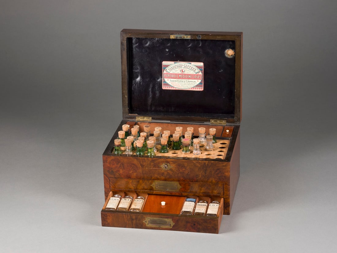 | REISEAPOTHEKE - HOMÖOPATHISCHE HAUSAPOTHEKE: REISEAPOTHEKE - HOMÖOPATHISCHE HAUSAPOTHEKE England, Ende 19. Jh. Glas, Korken, Holz, in Orig.-Kasten. 17 x 28,5 x 21,5 cm. Im Deckel Orig.-Etikett 'Thompson & Capper Liverpool, Manchester,