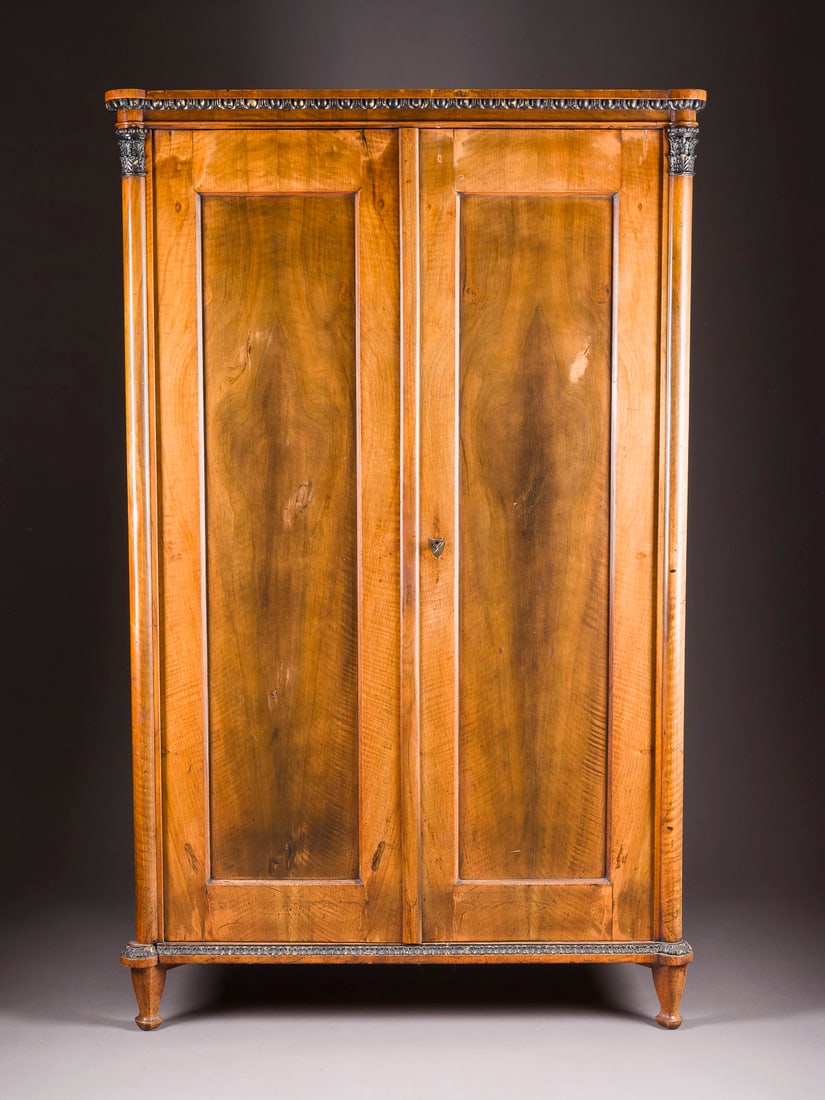 | BIEDERMEIER SCHRANK: BIEDERMEIER SCHRANK Österreich, um 1820 Mahagoni, Nussbaum, zweitürig, mit Schlüssel, geschnitzte, umlaufende Zargen. H. 169,5, B. 105, T. 47 cm. Part. best. und min. besch.BIEDERMEIER SCHRANK