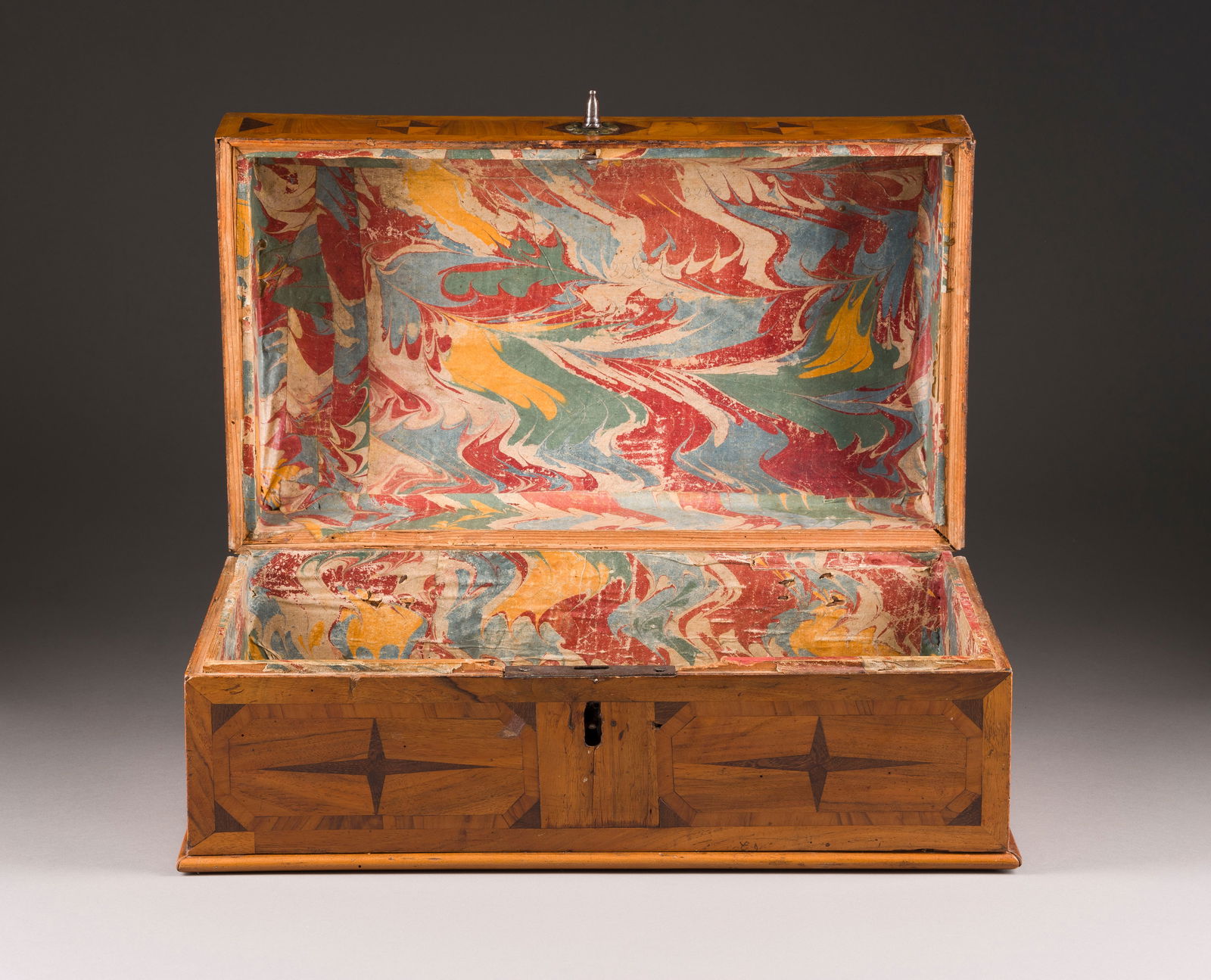 | KLEINE BIEDERMEIER TRUHE: KLEINE BIEDERMEIER TRUHE Deutsch, um 1820 Nussbaum, furniert, rechteckiger Korpus, Sternintarsien, flach gewölbter Deckel, aufklappbar. H. 21, B. 43, T. 28 cm. Part. best., besch.,