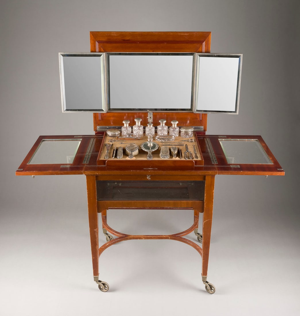 | ART DECO FRISIER VITRITENTISCH MIT 27 SILBEROBJEKTEN: ART DECO FRISIER VITRITENTISCH MIT 27 SILBEROBJEKTEN Deutsch, Berlin, Theodor Julius Gunther, um 1920 Mahagoni, geschliffenes Glas, Schminktisch auf vier Füßen, mit aufklappbaren Seiten und