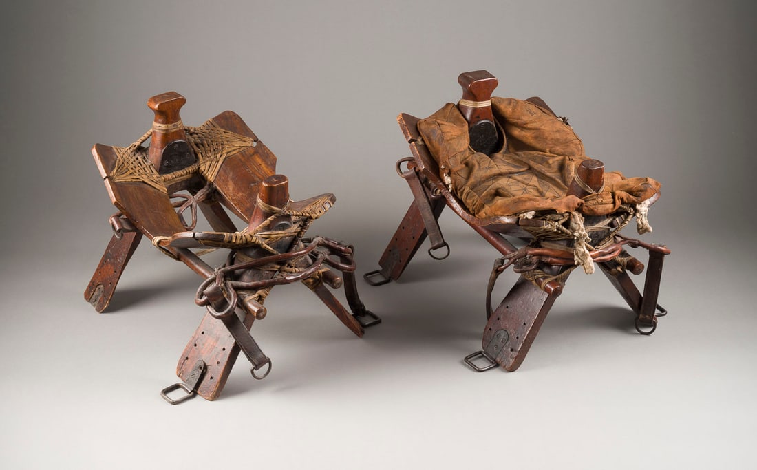 | PAAR KAMELSATTEL / -HOCKER: PAAR KAMELSATTEL / -HOCKER Wohl Marokko, 18./19. Jh. Holz, Leder und Lederriemen. H. ca. 53, B. 62, T. 46 cm. Part. best. und min. besch.PAAR KAMELSATTEL / -HOCKER