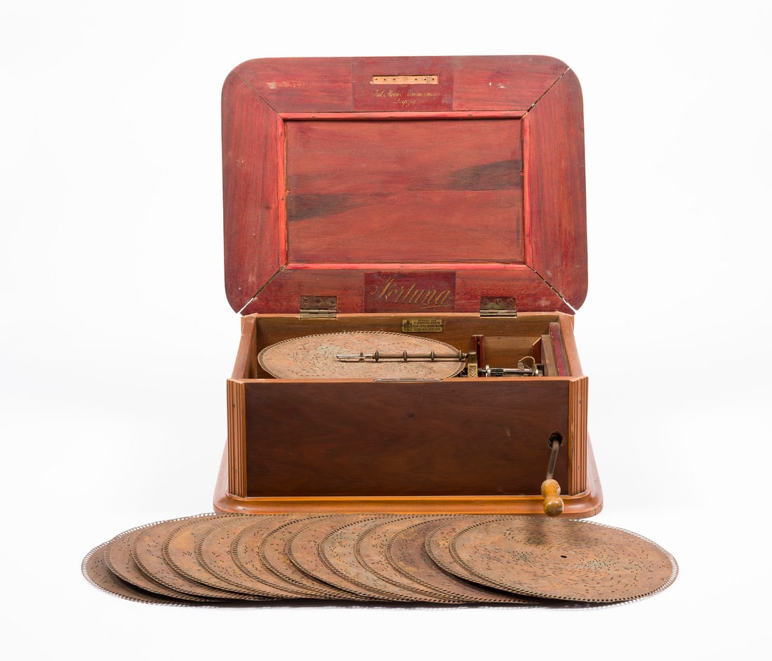 | LOCHPLATTENSPIELER 'FORTUNA' J. H. ZIMMERMANN: LOCHPLATTENSPIELER 'FORTUNA' J. H. ZIMMERMANN Leipzig, Anfang 20. Jh. Furniertes Holzgehäuse mit Kamm-Spielwerk, mechanisches Lochplatten-Spielwerk mit Kurbelantrieb. H. 21, B. 50, T. 38 cm. Innen be