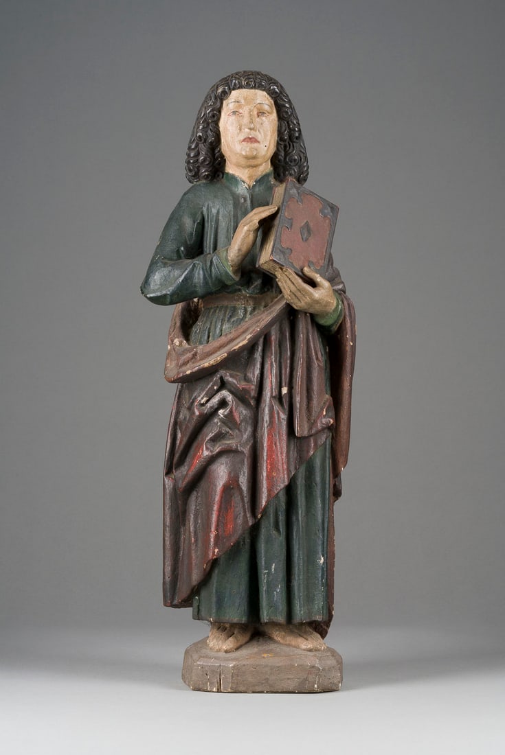 | STEHENDER APOSTEL MIT BUCH: STEHENDER APOSTEL MIT BUCH Rheinland, 18./19. Jh. Holz, plastisch geschnitzt, polychrom gefasst, Gipsauflage, auf einem Sockel. H. 69, B. 24, T. 18 cm. Part. best., besch. und rest., Fassungsverluste.