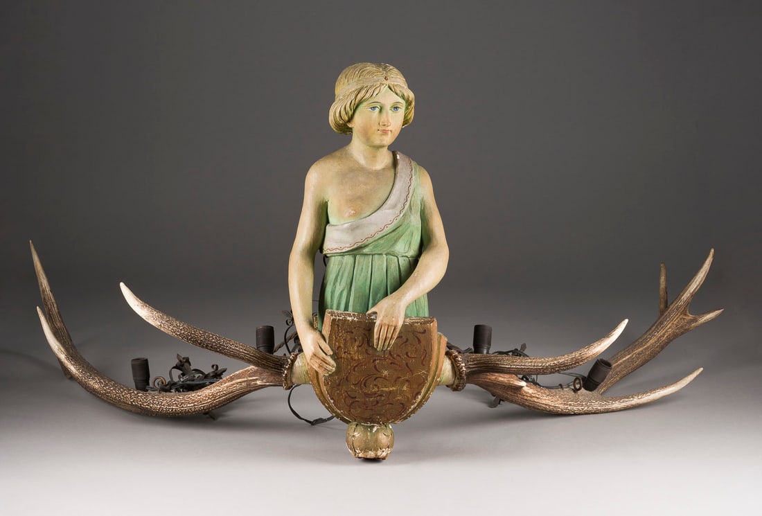 | LÜSTERWEIBCHEN MIT WAPPENSCHILD: LÜSTERWEIBCHEN MIT WAPPENSCHILD Deutsch, 19. Jh. Holz, plastisch geschnitzt, polychrom gefasst, vergoldet, Leuchterarme aus Gehörn. H. 61, B. 108, T. 80 cm. Schwebende Tragefigur