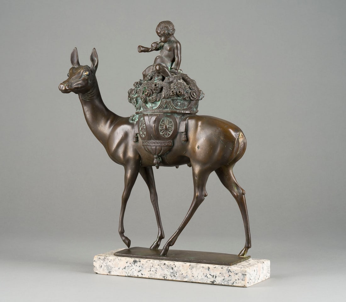 LUDWIG SONNLEITNER | PUTTO MIT BLASHORN AUF EINER HIRSCHKUH: LUDWIG SONNLEITNER 1878 Landau (Isar) - 1947 Würzburg PUTTO MIT BLASHORN AUF EINER HIRSCHKUH Bronze, dunkel patiniert, Glasaugen, auf rechteckiger Plinthe und Steinsockel (H. 3,5 cm). Ges.- H. 43, B.