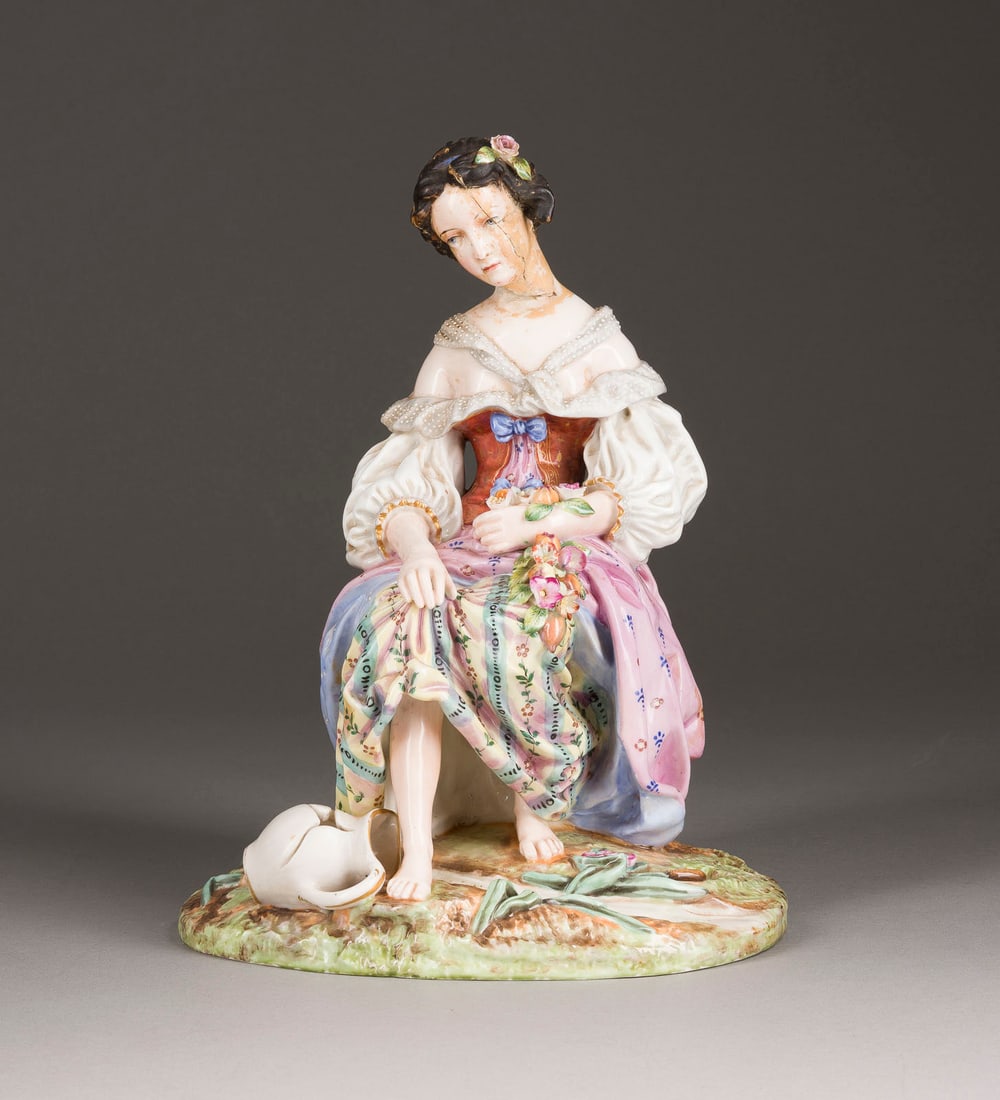| SITZENDE JUNGE FRAU MIT ZERBROCHENER KANNE: A PORCELAIN FIGURE OF A SITTING YOUNG LADY WITH A BROKEN JUG Russian, Volokiteno near Chernigov, Miklashevsky Pocelain Factory, 1850s Painted. Red factory mark 'AM'. Head chipped. 29.5 cm