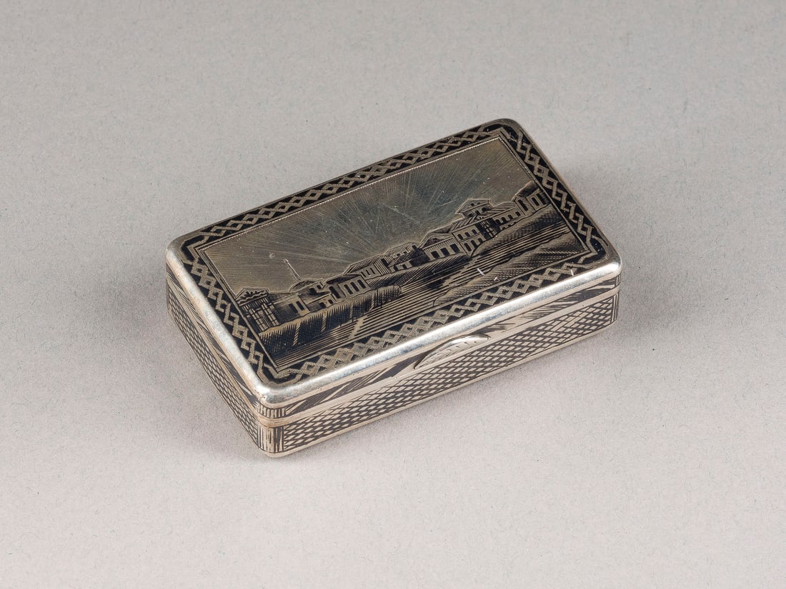 | NIELLO-SCHNUPFTABAKDOSE MIT PETERSBURGER ARCHITEKTURANSICHT: A SILVER AND NIELLO SNUFF BOX WITH AN ARCHITECTURAL VIEW OF ST. PETERSBURG Russian, Moscow, 1865 Of rectangular form. The hinged lid with architectural view. Marked with city hallmark, assayer's mark,