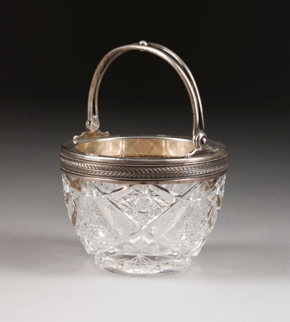 | KLEINE HENKELSCHALE: A SMALL SILVER-MOUNTED CUT-GLASS BOWL WITH HANDLE Russian, St. Petersburg, Alexander Karpov, 1908-1917 The silver mount embossed with laurel foliage. Marked with assayer's mark, 84 standard and master