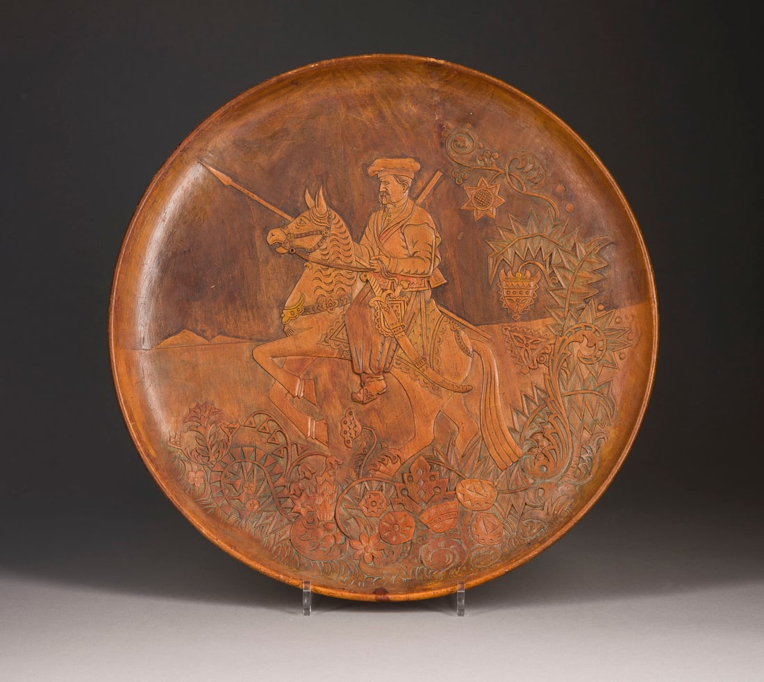 | GROSSER TELLER MIT TUeRKISCHEM REITER: A LARGE WOODEN PLATTER SHOWING A TURKISH HORSEMAN Probably Russian, around 1900 Carved, remains of paint. Diam 47 cm.GROSSER TELLER MIT TUeRKISCHEM REITER Wohl Russland, um 1900 Holz, geschnitzt,