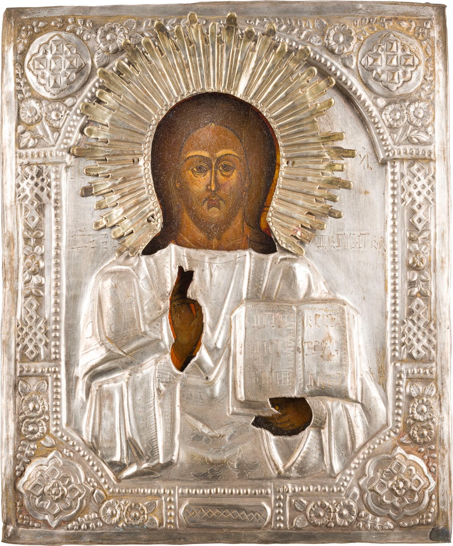 | IKONE MIT CHRISTUS PANTOKRATOR MIT OKLAD: AN ICON SHOWING CHRIST PANTOKRATOR WITH OKLAD Russian, 19th century Tempera on wood panel. Overlaid with a chased brass oklad. Vertical crack, partially restored. 31.2 x 26 cm.IKONE MIT CHRISTUS PANTO