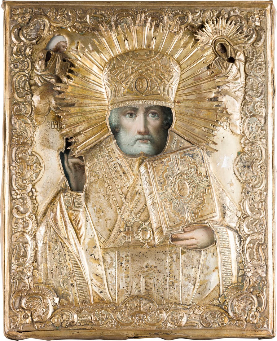 | GROSSE IKONE MIT DEM HEILIGEN NIKOLAUS VON MYRA MIT OKLAD: A LARGE ICON SHOWING ST. NICHOLAS OF MYRA WITH OKLAD Russian, mid 19th century Oil on wood panel with velvet backing. The brass oklad chased and repousse with rocailles motifs. Minor damages to the ed