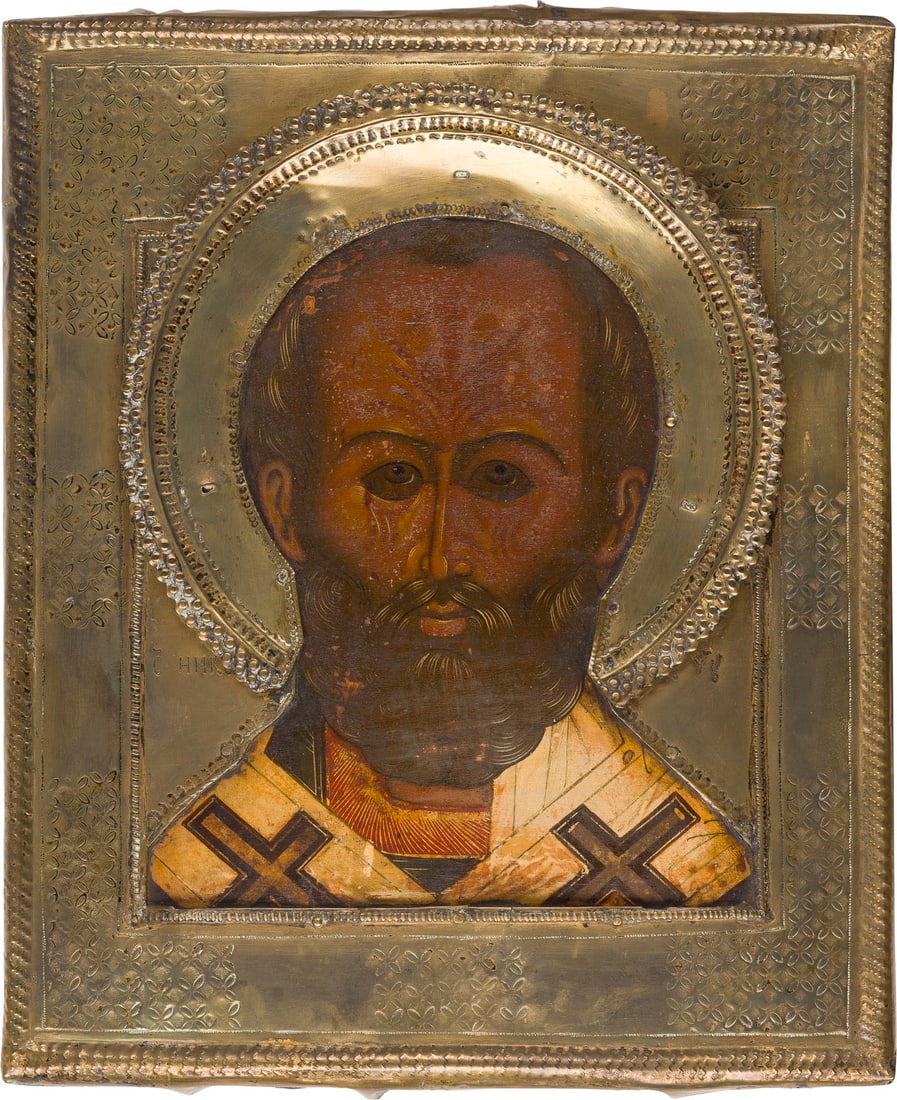 | IKONE MIT DEM HEILIGEN NIKOLAUS VON MYRA MIT RIZA: AN ICON SHOWING ST. NICHOLAS OF MYRA WITH RIZA Russian, 18th century in the style of the 16th century Tempera on wood panel. The brass riza punched with foliage. Minimally restored. 31.3 x 26 cm.IKONE