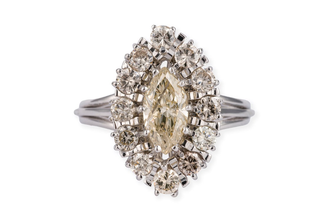 NAVETTE ENTOURAGE RING: NAVETTE ENTOURAGE RING WG 750. Ringmass: ca. 56. Ringkopfmasse: ca. 19,5 x 13,0 mm. Ges.-Gew.: ca. 5,6 g. Ring, besetzt mit einem zentralen Diamanten im Marquiseschliff von ca. 0.80 ct. L/P und einem 