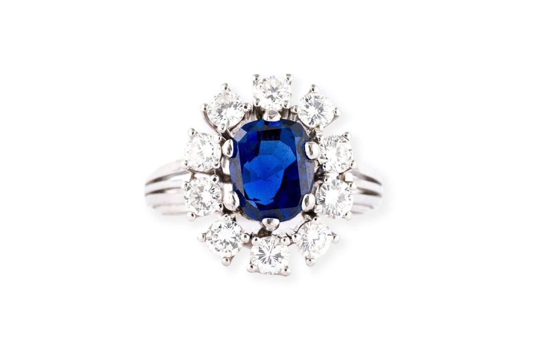 SAPHIR ENTOURAGE RING: SAPHIR ENTOURAGE RING WG 750. Ringmass: 58. Ringkopfmasse: 17,1 x 15,1 mm. Ges.-Gew.: ca. 6,8 g. Ring, besetzt mit einem zentralen Saphir von ca. 2.72 ct und einem Kranz aus Brillanten zus. ca. 1.35