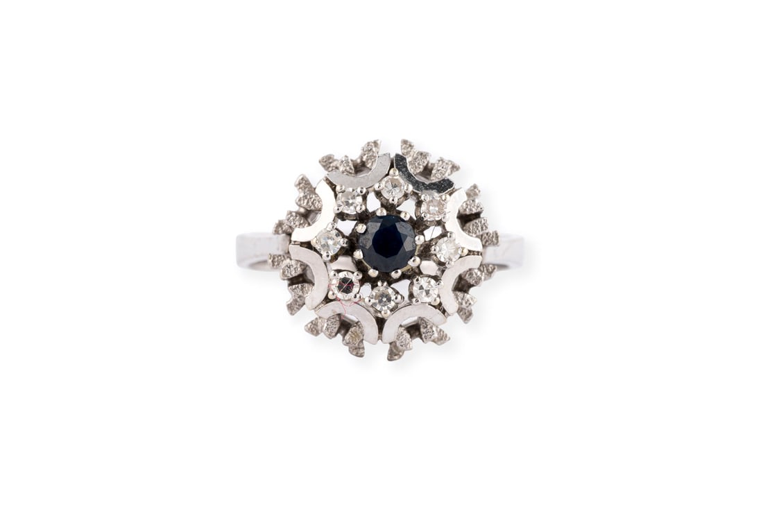 HOHER SAPHIR COCKTAIL RING: HOHER SAPHIR COCKTAIL RING WG 585. Ringmass: ca. 55. D.(Ringkopf): ca. 14,5 mm. Ges.-Gew.: ca. 5,6 g. Ring, besetzt mit einem zentralen Saphir von ca. 0.20 ct. und einem Kranz aus Diamanten im