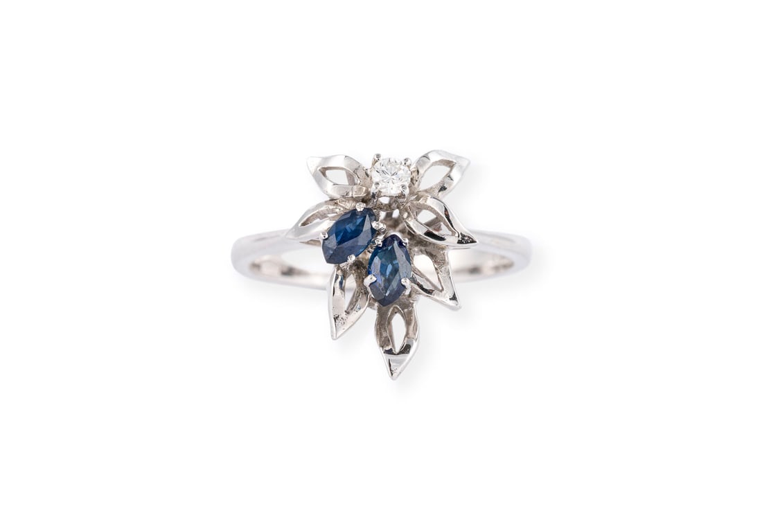 BLUETEN SAPHIR BRILLANT RING: BLUETEN SAPHIR BRILLANT RING WG 750. Ringmass: ca. 50. Ringbreite: ca. 13,7 mm. Ges.-Gew.: ca. 3,1 g. Ring, in zarter Bluetenform, besetzt mit einem kleinen Brillanten von ca. 0.04 ct. und 2 kleinen