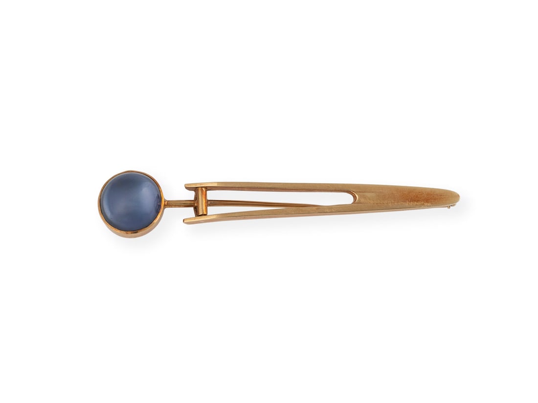 DESIGN BROSCHE: DESIGN BROSCHE GG 585. L.: ca. 7,7 cm. Ges.-Gew.: ca. 11,1 g. Mit blauem Stein unterlegter Bergkristall-Cabochon, Ges. ca. 12,7 x 5,8 mm.