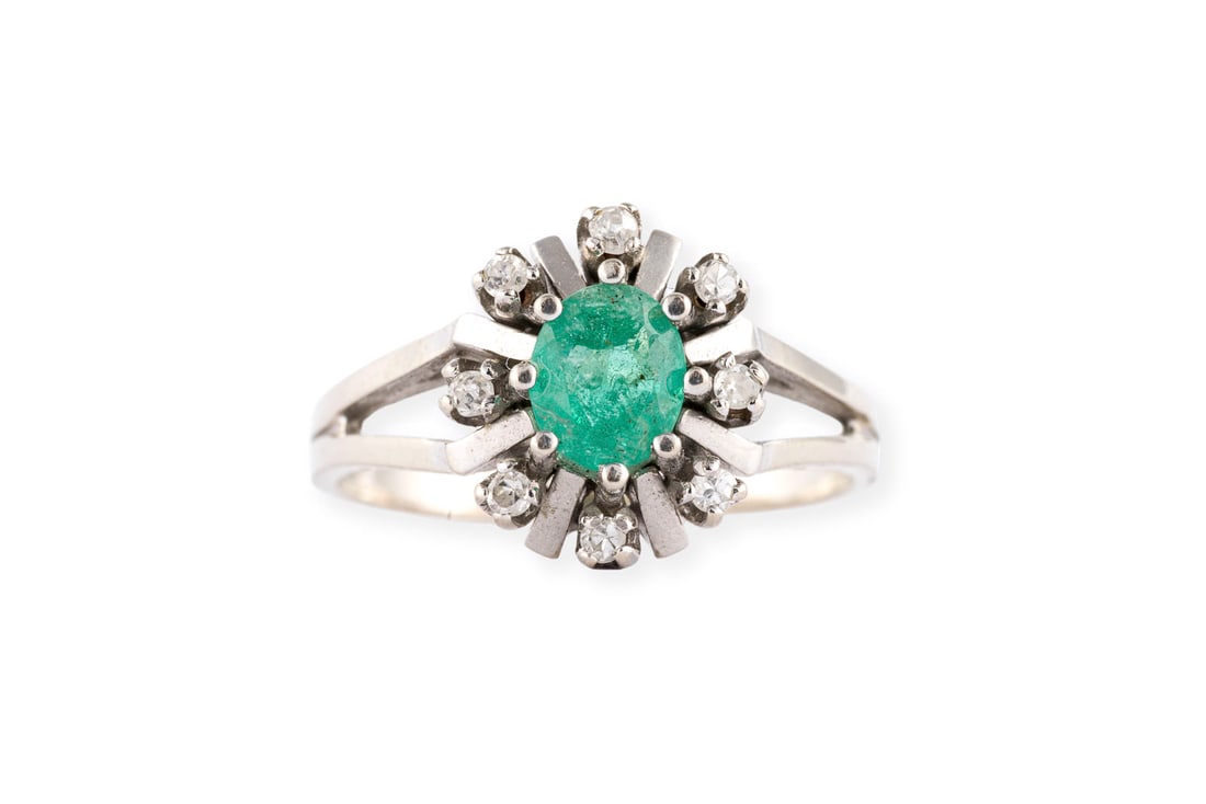 SMARAGD ENTOURAGE RING: SMARAGD ENTOURAGE RING WG 585. Ringmass: ca. 51. Ringkopfmasse: ca. 11,0 x 10,2 mm. Ges.-Gew.: ca. 3,6 g. Ring, besetzt mit einem zentralen Smaragd von ca. 0.35 ct. und einem Kranz aus kleinen