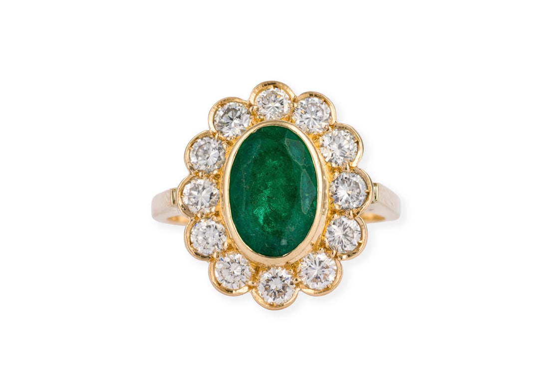 OVALER SMARAGD COCKTAIL RING: OVALER SMARAGD COCKTAIL RING GG 750. Ringmass: ca. 55. Ringkopfmasse: ca. 17,8 x 15,4 mm. Ges.-Gew.: ca. 6,2 g. Ovaler Ring, besetzt mit einem zentralen Smaragd von ca. 1.53 ct. und einem Kranz aus Br